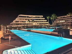 A swimming pool with a modern hotel building in the background. - LOLA Beachfront Garden Apartment | Pools, Direct Beach Access, and Family-Friendly (Torremolinos)