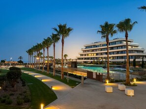 Ein modernes Hotel mit Pool, Palmen und einem gut beleuchteten Weg.