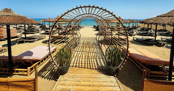 A beach with a wooden archway leading to the sea, surrounded by sun loungers and thatched umbrellas. - LOLA Beachfront Garden Apartment | Pools, Direct Beach Access, and Family-Friendly (Torremolinos)