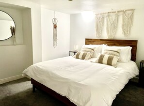 A neatly made bed with white bedding and patterned pillows, a bedside table with a lamp, and a wall-mounted macrame piece. - North Bay Nest - Luxury Holiday Apartment - 5 Minute Walk From The Beach (Scarborough)