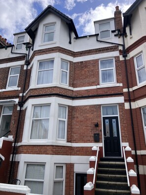 A multi-story residential building with a black front door, white-framed windows, and a brick facade. - North Bay Nest - Luxury Holiday Apartment - 5 Minute Walk From The Beach (Scarborough)