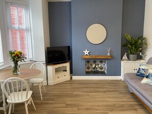 A living room with a TV on a stand, a fireplace, a sofa, a dining table with chairs, and a potted plant. - North Bay Nest - Luxury Holiday Apartment - 5 Minute Walk From The Beach (Scarborough)