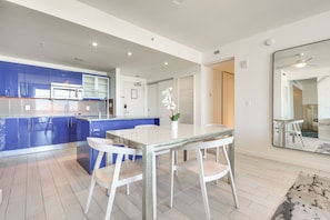 A modern kitchen with blue cabinets, a white dining table, and a large mirror. - 3 High-rise Beach Condos! Views, Resort Perks (Fort Lauderdale)