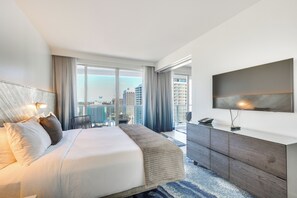 Una camera d'albergo moderna con un letto grande, una televisione a schermo piatto, vista sulla città e un balcone con zona pranzo.