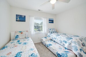A bedroom with two single beds, a ceiling fan, and a window with blinds. - Saltwater Revival - Stay with Seaside Vacations! (Chincoteague Island)