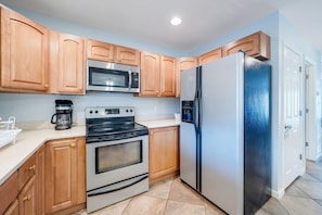 A kitchen with wooden cabinets, a stainless steel microwave, a refrigerator, an oven, and a coffee maker. - Saltwater Revival - Stay with Seaside Vacations! (Chincoteague Island)