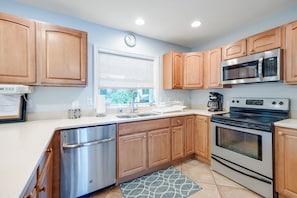 A modern kitchen with wooden cabinets, stainless steel appliances, a dishwasher, and a clock on the wall. - Saltwater Revival - Stay with Seaside Vacations! (Chincoteague Island)