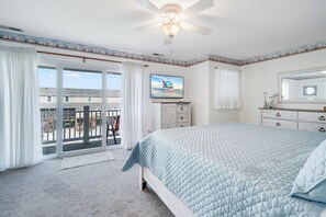 A bedroom with a bed, a ceiling fan, a television, and a view of the outside. - Saltwater Revival - Stay with Seaside Vacations! (Chincoteague Island)