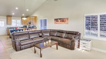 A spacious living room with a large leather sectional sofa, a wooden coffee table, and a view of the kitchen in the background.