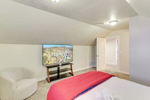 Ein Schlafzimmer mit einem Bett, einem an der Wand montierten Fernseher, einem Sessel und einer Tür.