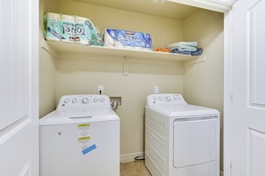 A laundry room with two front-loading washing machines, a shelf with toilet paper, and a small storage area.