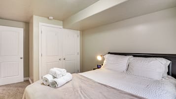 A bedroom with a bed, two white doors, a nightstand with a lamp, and a rolled-up towel on the bed.
