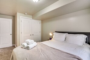 A bedroom with a bed, two white doors, a nightstand with a lamp, and a rolled-up towel on the bed. - Patio & Mtn Views! Group Getaway in South Jordan (South Jordan)