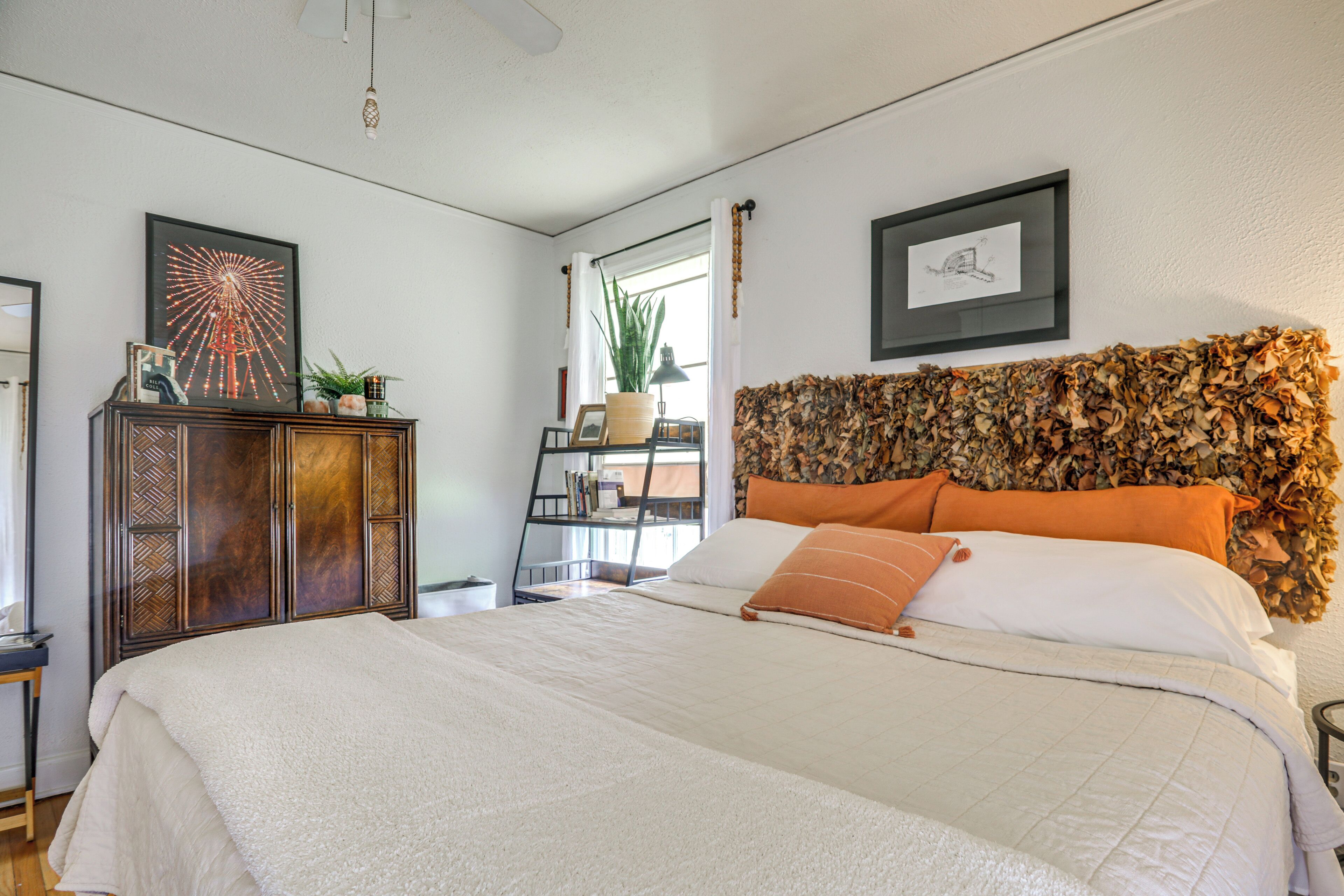 A bedroom with a large bed, a wooden headboard with a leaf pattern, a side table, a dresser, and a framed picture on the wall.