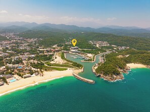An aerial view of a coastal area with a marina, a beach, and a dense forested area. - Stylish 2BR | Beach & Town Nearby | 2nd Level (Huatulco)