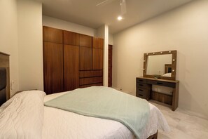 A bedroom with a bed, a wooden wardrobe, a vanity with a mirror, and a small plant. - Stylish 2BR | Beach & Town Nearby | 2nd Level (Huatulco)