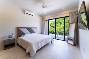 A bedroom with a bed, bedside table, air conditioning unit, ceiling fan, and a view of greenery through a sliding glass door. - Stylish 2BR | Beach & Town Nearby | 2nd Level (Huatulco)