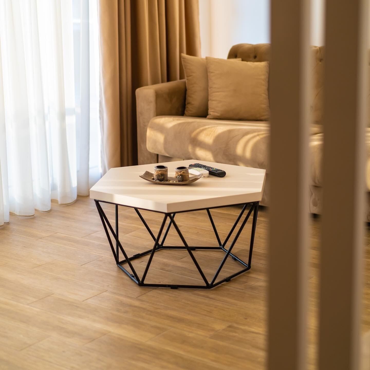 Une pièce avec une table basse ronde, dotée d’un cadre en métal aux motifs géométriques, une télécommande et un plateau sur lequel reposent deux bougies.