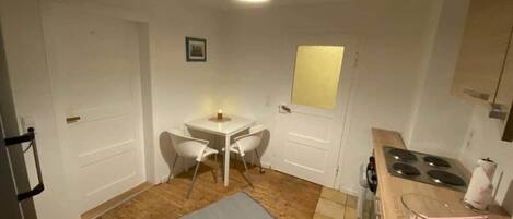 A compact kitchen with a dining table, chairs, a stove, and a small refrigerator.