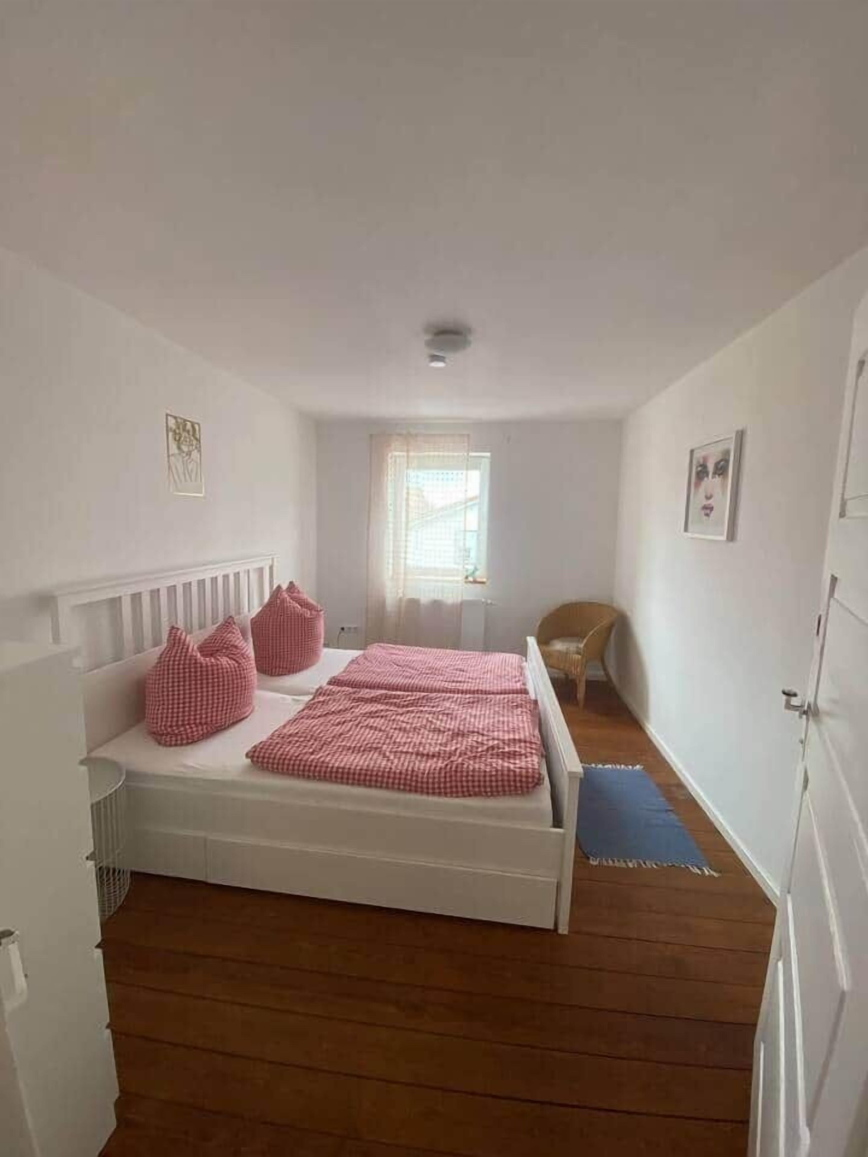 Ein Schlafzimmer mit einem Einzelbett, einem Sessel, einem Fenster und einer Tür.