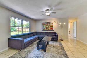A living room with a sectional sofa, a coffee table, a floor lamp, a ceiling fan, and a large window with a view of greenery. - 6 Mi to Dtwn! Centrally Located Sarasota Home (Sarasota)