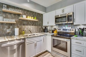 A modern kitchen with stainless steel appliances, white cabinetry, and a granite countertop. - Near Grand Boulevard & Beaches! Coastal Condo (Miramar Beach)