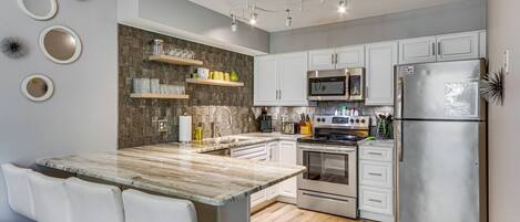 A modern kitchen with a central island, white cabinetry, stainless steel appliances, and decorative wall mirrors.