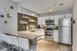 A modern kitchen with a central island, white cabinetry, stainless steel appliances, and decorative wall mirrors. - Near Grand Boulevard & Beaches! Coastal Condo (Miramar Beach)
