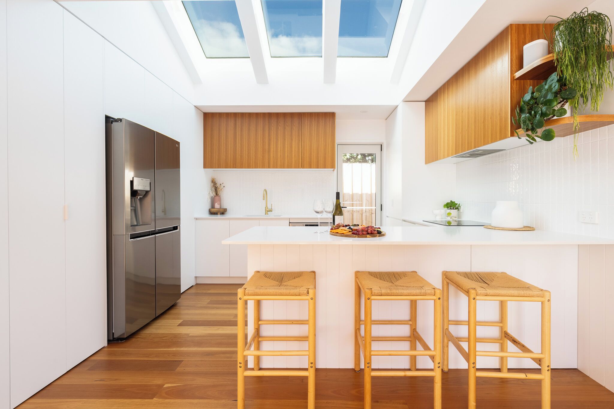 Eine moderne Küche mit einer zentralen Kochinsel, Holzbarhocker, einem Edelstahlkühlschrank und einem Oberlicht.