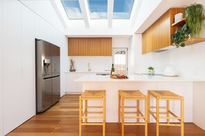 Eine moderne Küche mit einer zentralen Kochinsel, Holzbarhocker, einem Edelstahlkühlschrank und einem Oberlicht.