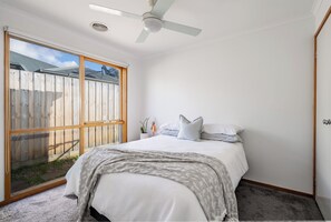 A bedroom with a bed, a ceiling fan, a window, and a view of a wooden fence. - Coastal 4BR with pool, walk to Ocean Grove beach (Ocean Grove)