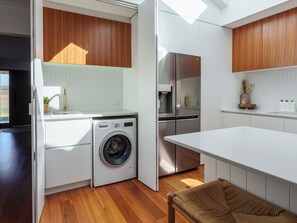 A compact kitchen with a washing machine, a refrigerator, and a dining area. - Coastal 4BR with pool, walk to Ocean Grove beach (Ocean Grove)