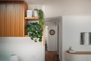 A modern kitchen with white cabinetry, a wooden accent panel, a hanging plant, and a built-in speaker. - Coastal 4BR with pool, walk to Ocean Grove beach (Ocean Grove)