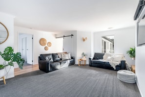 Ein modernes Wohnzimmer mit zwei schwarzen Ledersofas, einem grauen Teppich und einem großen Fenster.