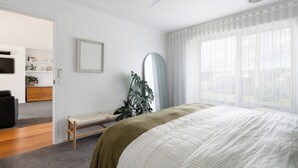 Een slaapkamer met een bed, een bankje, een spiegel en een plant.