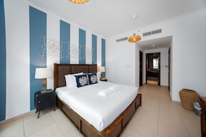 Habitación de hotel con una cama grande, una mesita de noche, un adorno en la pared y un pasillo que conduce a otra habitación.