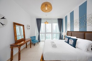 Ein Hotelzimmer mit einem großen Bett, einem Nachttisch aus Holz, einem blauen Stuhl, einem großen Fenster mit Vorhängen und einem dekorativen Wandbild.