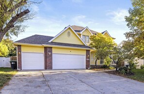 Uma casa residencial de dois andares com garagem, jardim frontal e uma árvore.