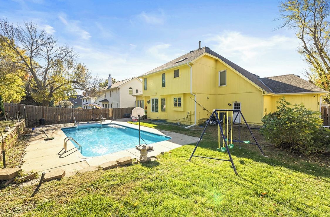 Un jardin à l’arrière d’une maison d’habitation, avec une piscine, une balançoire et la maison elle-même.