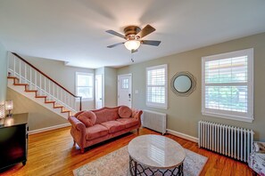 A living room with a staircase, a pink sofa, a round coffee table, and a ceiling fan. - 1 Mi to Trolley Square! Family Home w/ Bar & Yard (Wilmington)