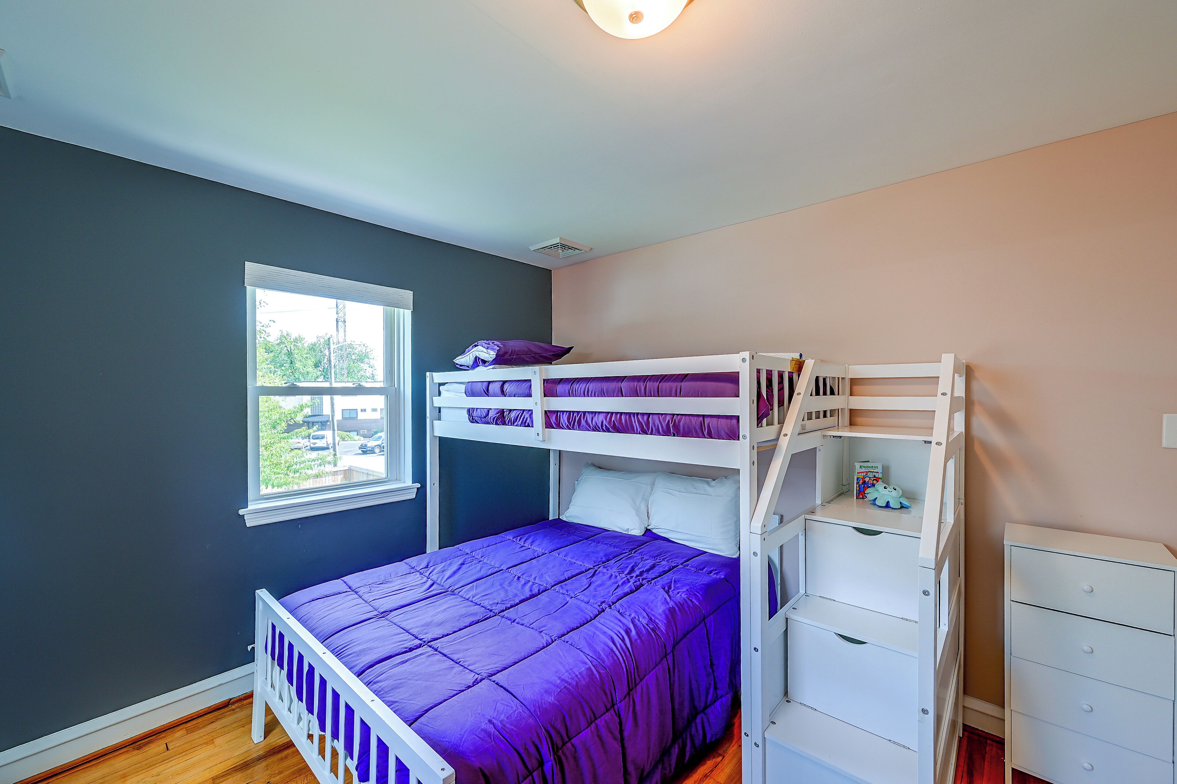 A room with a bunk bed, a window, and a dresser.