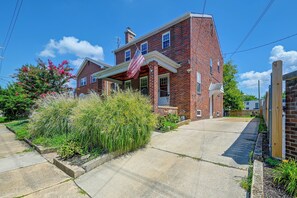 A two-story brick house with a front porch, a small attached garage, and a well-maintained garden with various plants and flowers. - 1 Mi to Trolley Square! Family Home w/ Bar & Yard (Wilmington)