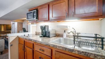 A kitchen with wooden cabinets, a microwave, a toaster, and a sink with a dish rack.