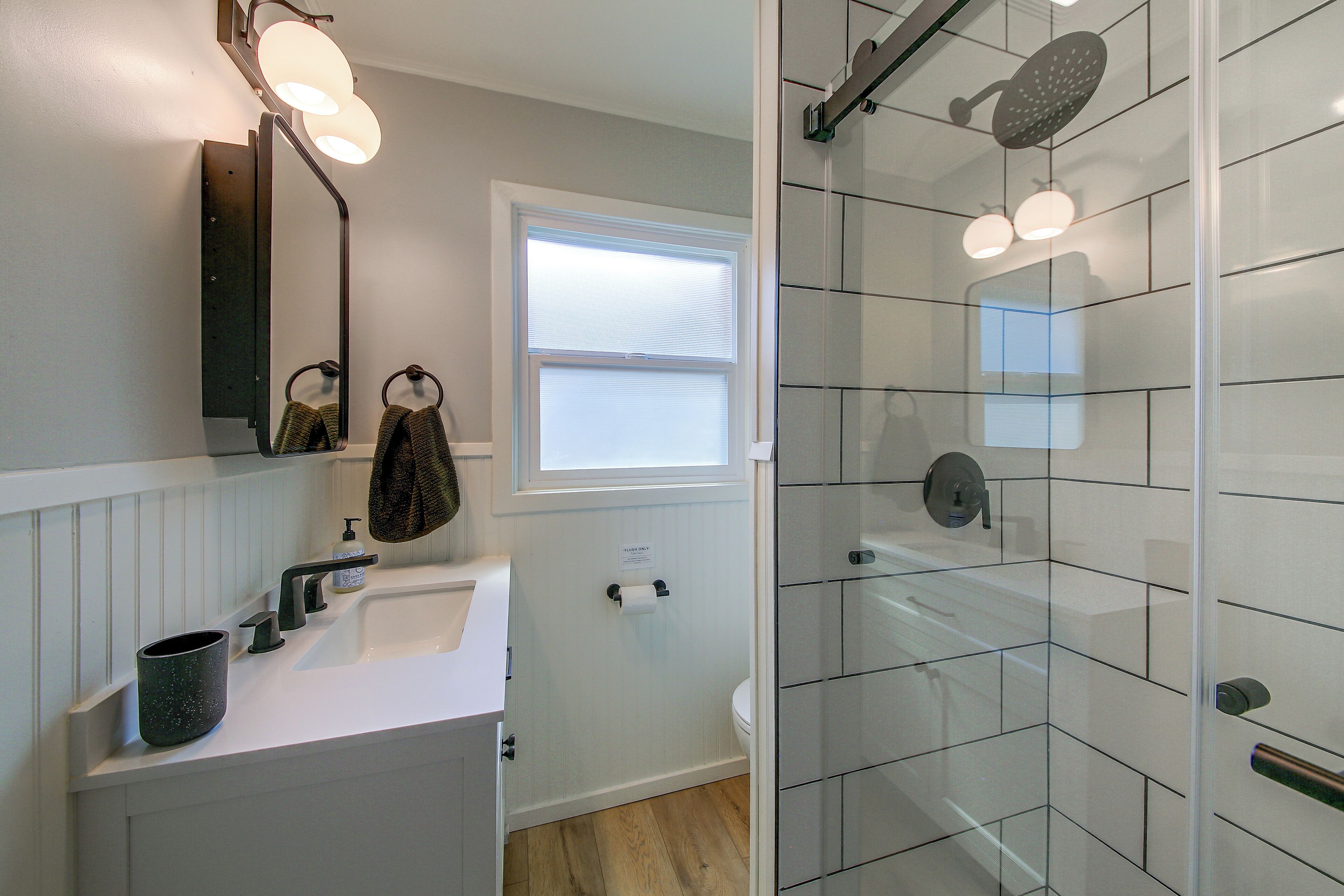 A bathroom with a white sink, a mirror, a towel, a glass shower enclosure, and a toilet.