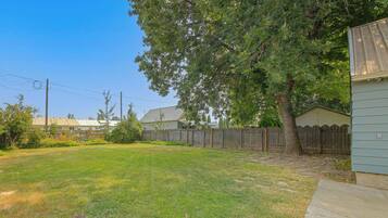 Un patio trasero residencial con césped, cerca de madera y un árbol grande.