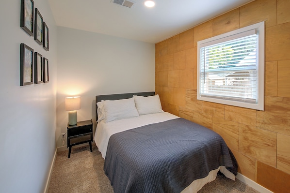 Un dormitorio con cama, mesita de noche, lámpara y ventana con persianas.