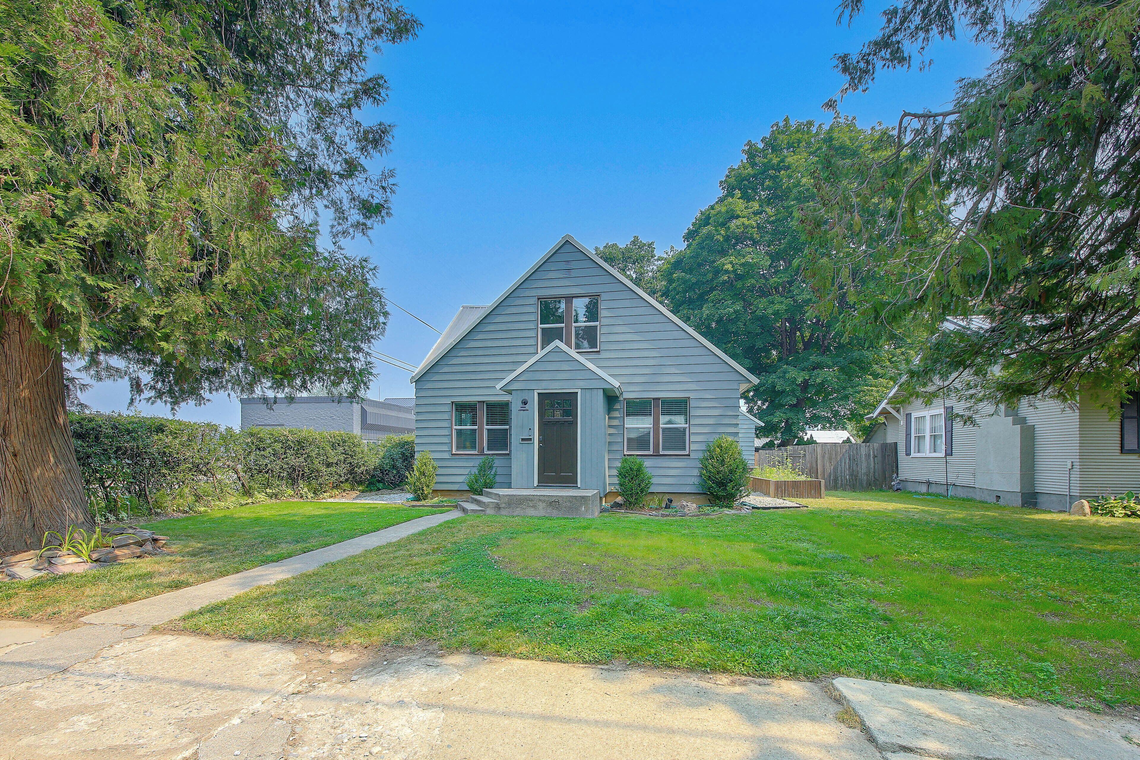 A single-story house with a front porch, a small front yard, and a large tree to the left.