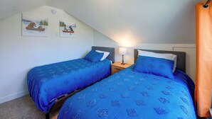 Habitació amb dos llits, una làmpada al sostre i dos quadres penjats a la paret.
