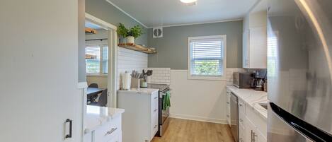 A kitchen with white cabinets, a stainless steel refrigerator, a wooden countertop, and a potted plant on the wall.