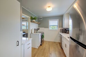 Una cocina con armarios blancos, un refrigerador de acero inoxidable, una encimera de madera y una planta en maceta en la pared.